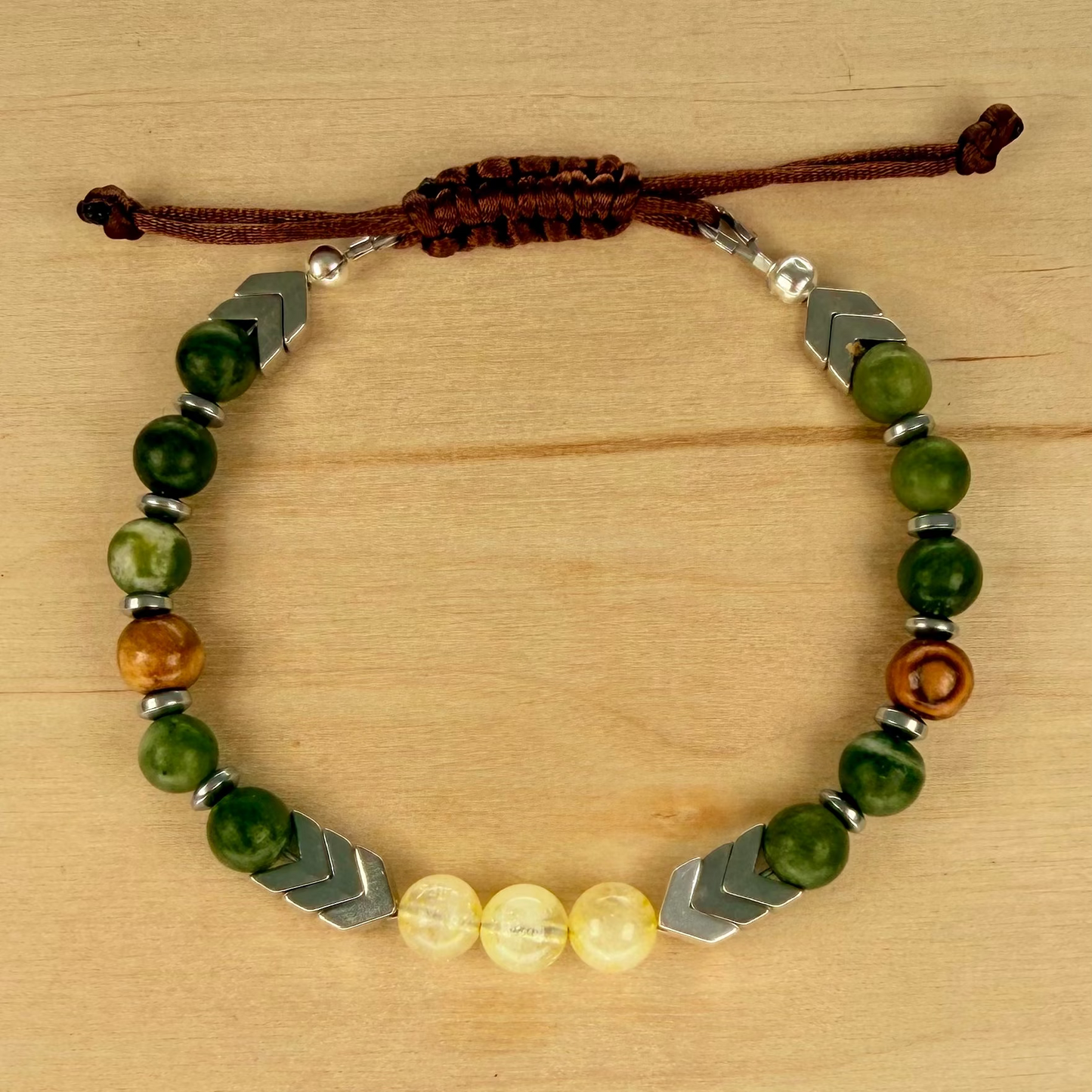 Bracelet with green beads, brown cord, and silver accents on a wooden surface