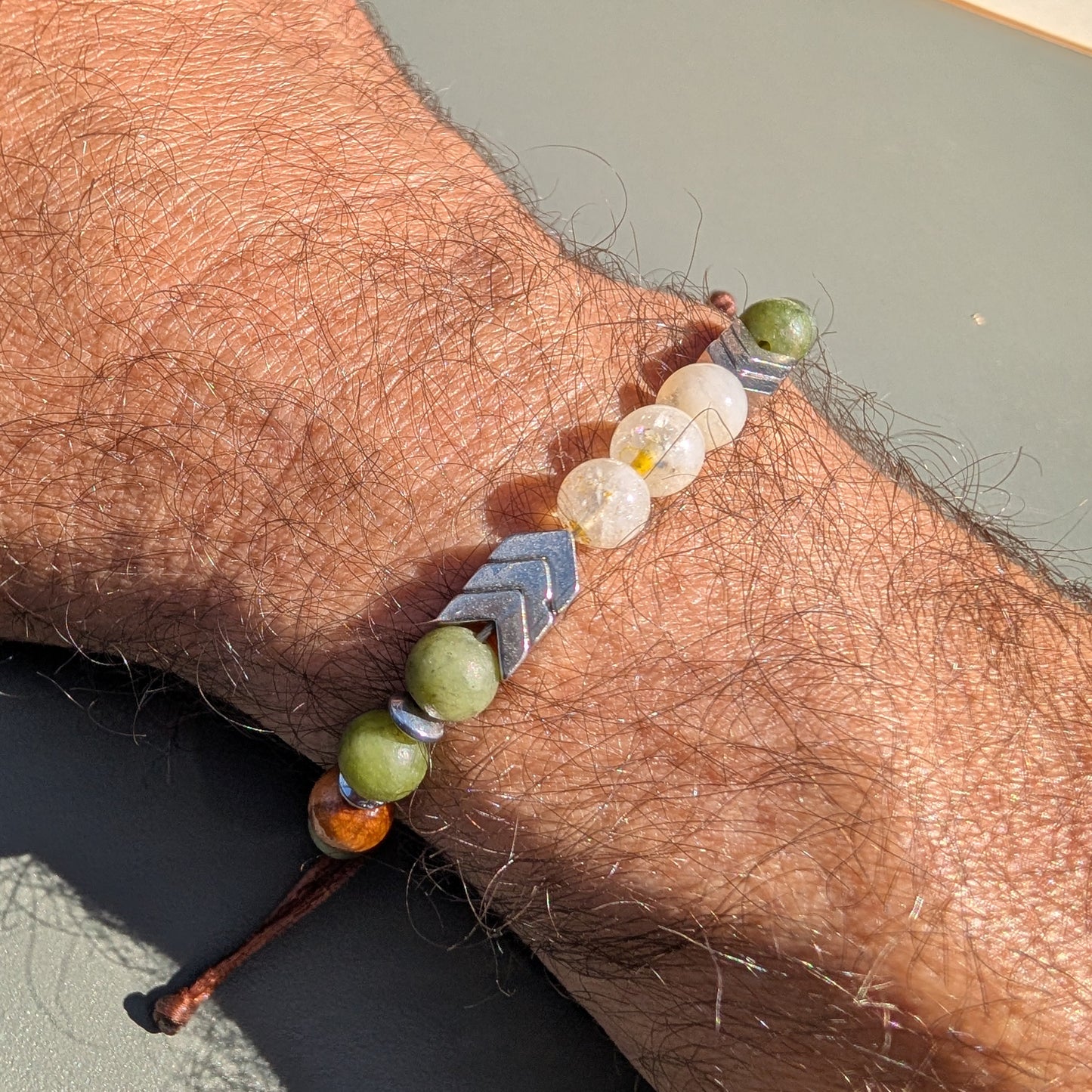 Bracelet with green beads and a silver arrowhead charm on a wrist against a neutral background