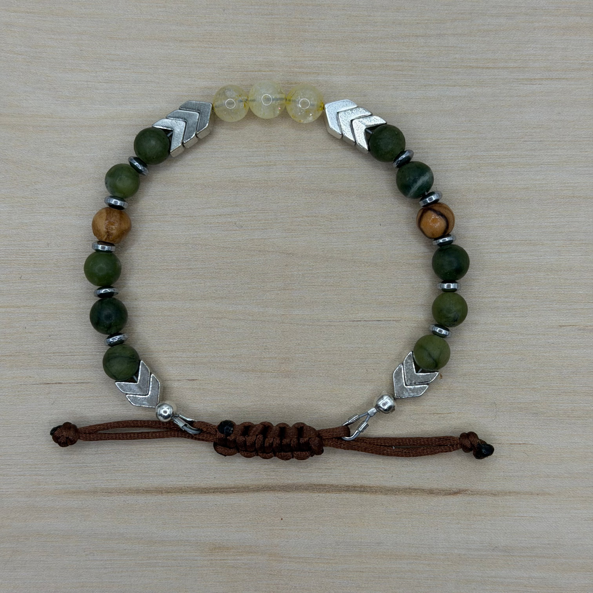 Bracelet with green, brown, and silver beads on a wooden surface